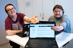 Kaksi miestä istuvat pöydän ääressä ja osoittavat toisella kädellä pöydällä olevaa tietokoneen ruutua.