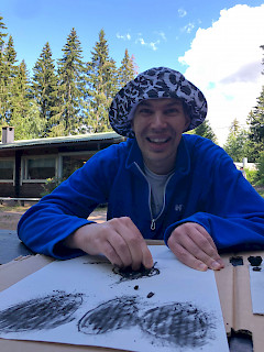 nuori mies piirtää hiilellä kuvaa kesäinen hattu päässä aurinkoisessa säässä