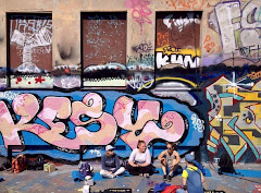 kuvassa istuu maassa nuoria, taustalla talon seinässä on graffittimaalauksia