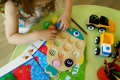 Tyttö istuu pöydän ääressä ja leikkii värikkäillä leluilla.