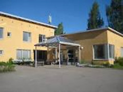 Keltainen talo ja asfalttipiha. Talossa sijaitsee Oskarinpuiston toimijatalo.