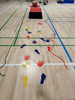 Liikuntasali, jossa lattialla erivärisiä jalan ja käden muotoisia kuvioita. Takana temppupatja.