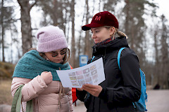 Kaksi kaveria tutkii yhdessä paperia, jossa on luontobongaustehtävä. Taustalla on keväinen luonto.