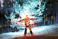 Talvella lumisessa ympäristössä otettu valomaalaus henkilöstä, johon kohdistettu valoja ja luminen puu heijastuu taustalla.