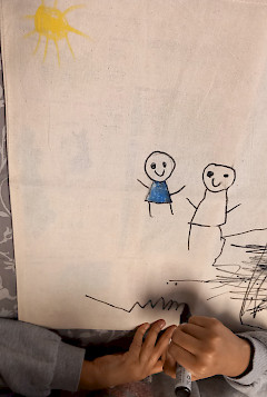 Kuvassa on kaksi tikku-ukkoa, keltainen aurinko ja lapsen kädet.