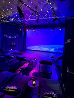 Kuva elokuvasalista, jossa sininen sävy, valkokangas ja tuoleja.