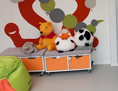 Kuvassa näkyy kuviollisen seinän edessä neljä pehmolelua, jotka ovat säilytyssenkin päällä. Kuvassa näkyy myös pikkuisen kaksi säkkituolia, jotka ovat väriltää vaaleanvihreä ja oranssi.