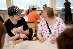 Mies ja nainen juttelevat pöydän ääressä ja tekevät yhdessä taidetyöskentelyä