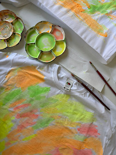 T-paita on maalattu kangasväreillä ja paidan vieressä värejä ja siveltimet