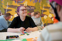 Nuori nainen istuu hymyillen pöydän ääressä ja tekee taidetyötä