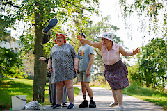 Nuori nainen heittää saapasta aurinkoisessa säässä kahden muun henkilön kannustaessa