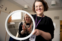 Nuori nainen katsoo peilistä, jota toinen nainen pitelee kädessään.