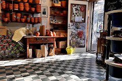 Keramiikkastudio, hyllyillä ruukkuja, mustavalkokuvioinen lattia.