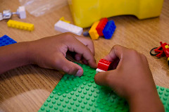 Kuvassa kaksi kättä, jotka rakentavat legopalikoilla