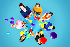 Seitsemän henkilöä seisoo ringissä ja heittää jonglöörauspalloja kohti kuvaajaa.