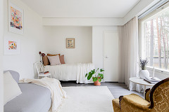 Valoisa asunto, jossa sohva, sänky, nojatuoli ja kasveja.